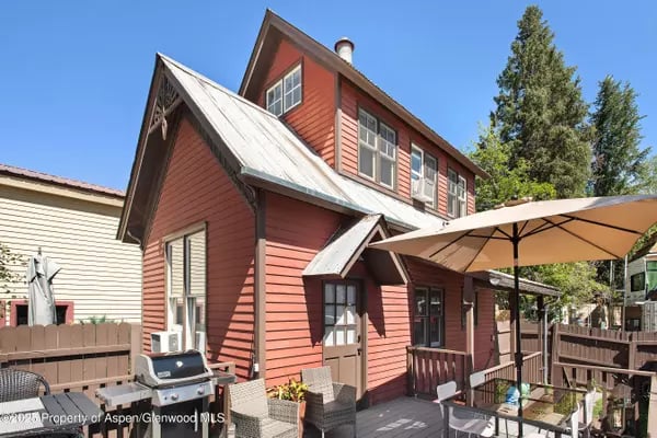 Red multi-story house with steep metal roofs and a deck shaded by a tan patio umbrella.
