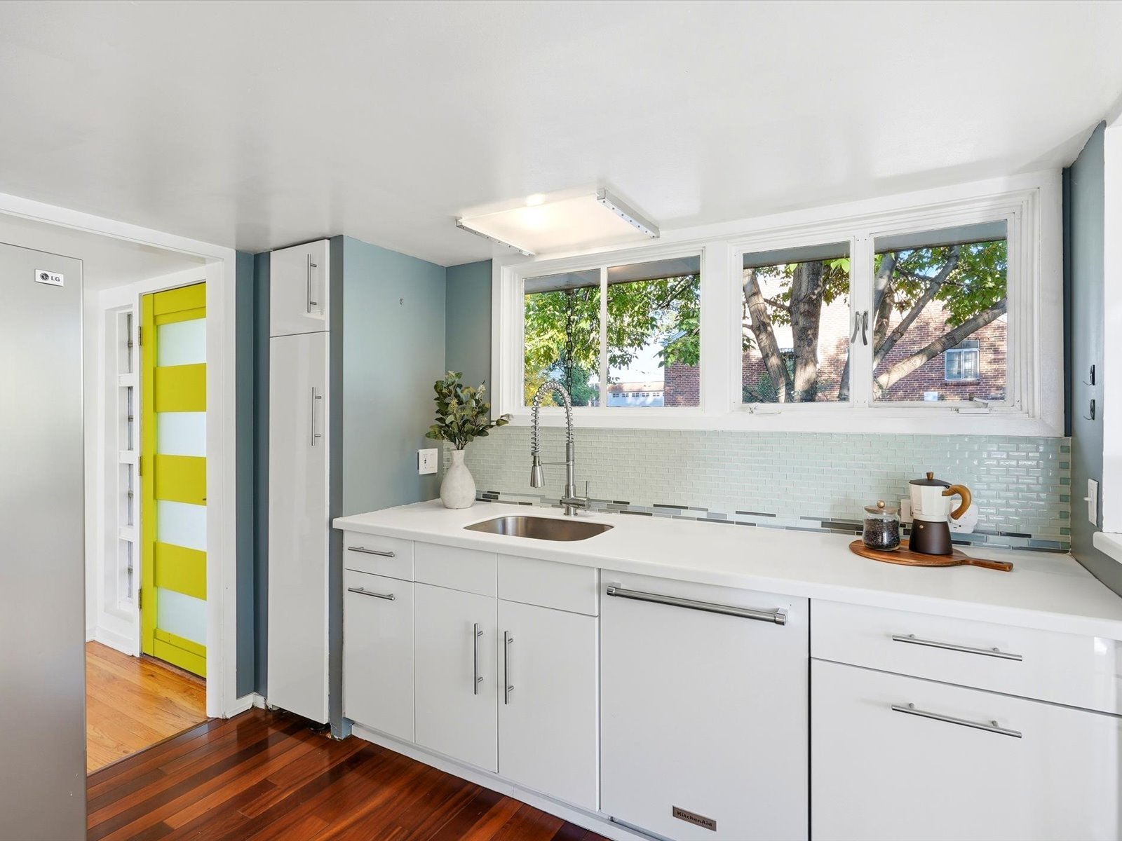 Modern kitchen with pale aqua tile backsplash, wide windows, and a vivid yellow-and-white striped door.