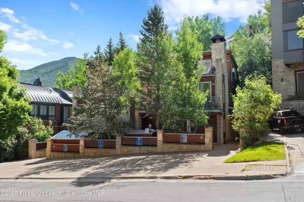 Aspen homes with brick facades and balconies, framed by leafy trees and a wooded mountain.