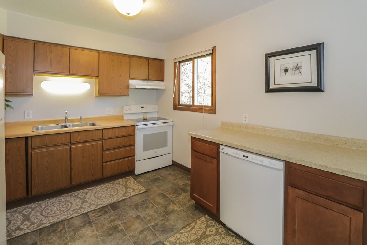 Kitchen with wood cabinets, white appliances, dark tile flooring, and patterned rugs.