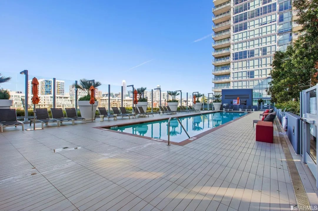 A wide view of the rooftop swimming pool at Arden Residences surrounded by lounge chairs and umbrellas.