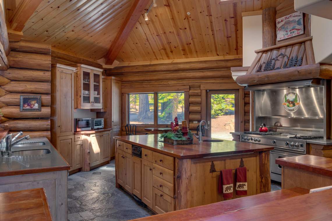 Rustic log-home kitchen with a large island, vaulted wood ceiling, and professional stainless-steel range.