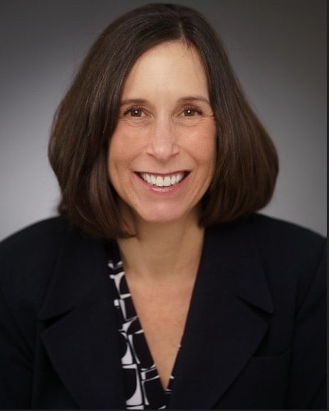 Erica Long smiling in a black blazer and patterned blouse.