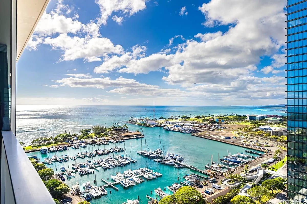 High-rise balcony view over a boat-filled marina and turquoise harbor toward the ocean.