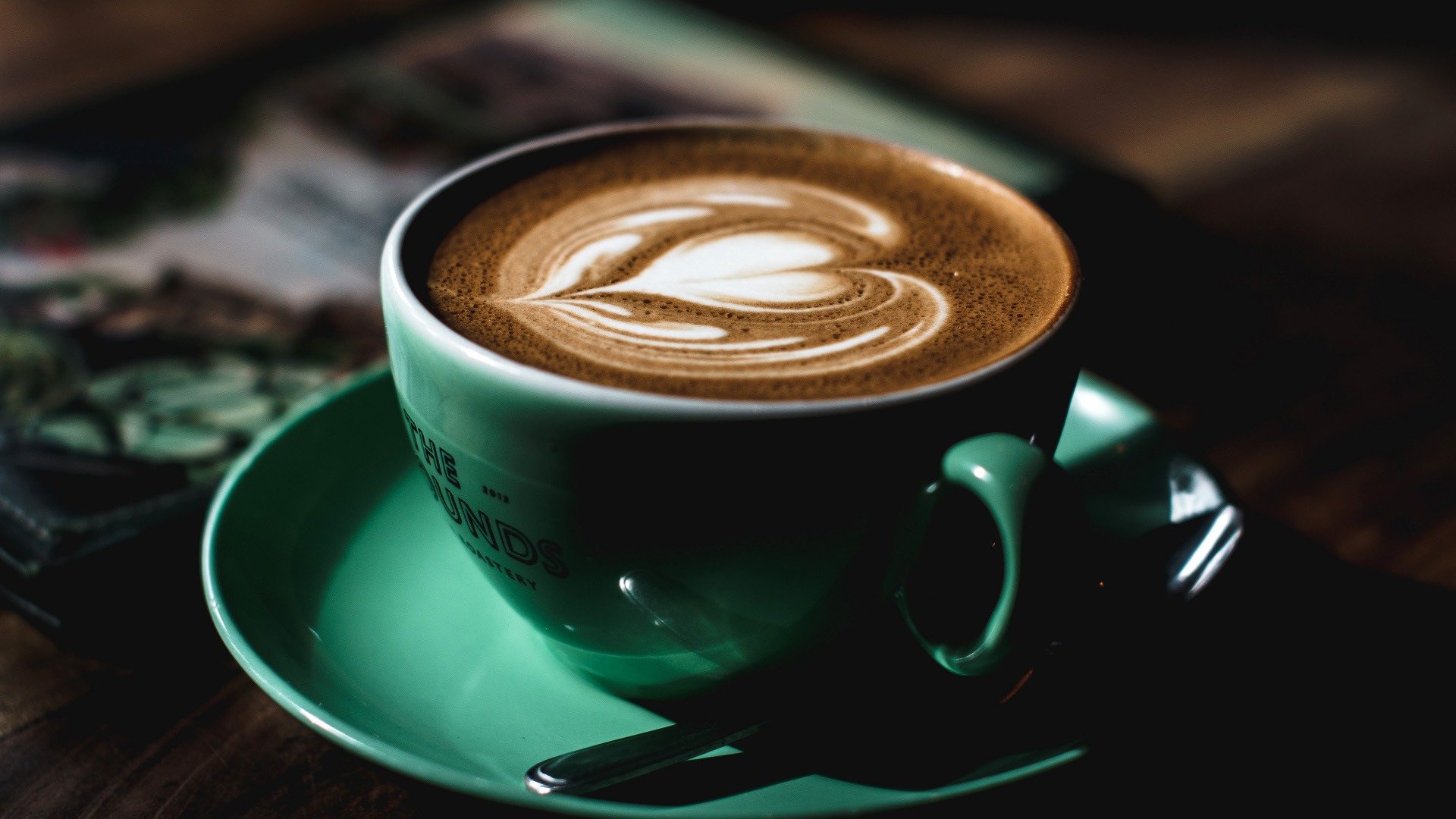 Latte with leaf-shaped foam art in a green cup and saucer.