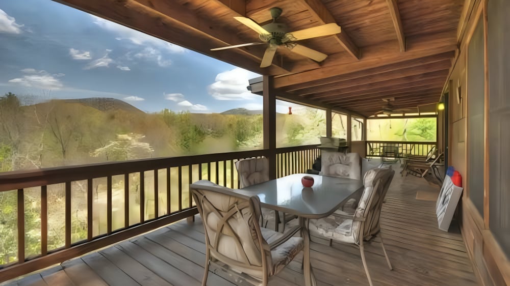 Covered deck with outdoor dining set and views of wooded hills and distant mountains.