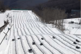 Snow-covered ski slope with parallel groomed runs and wooded hillsides.