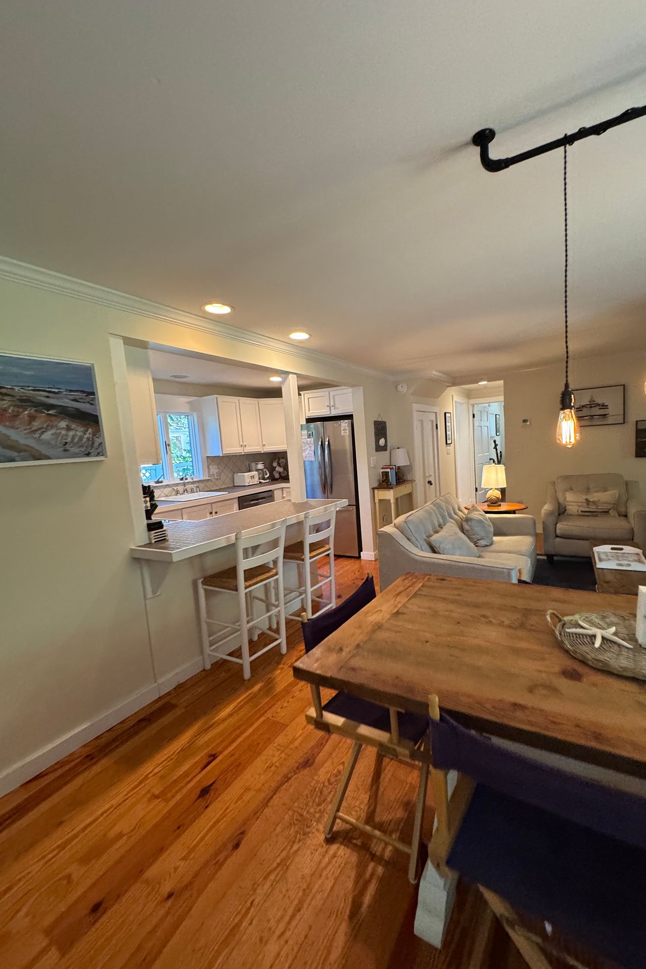 Open-plan kitchen and living room with a breakfast counter, hardwood floors, and a large wooden dining table.