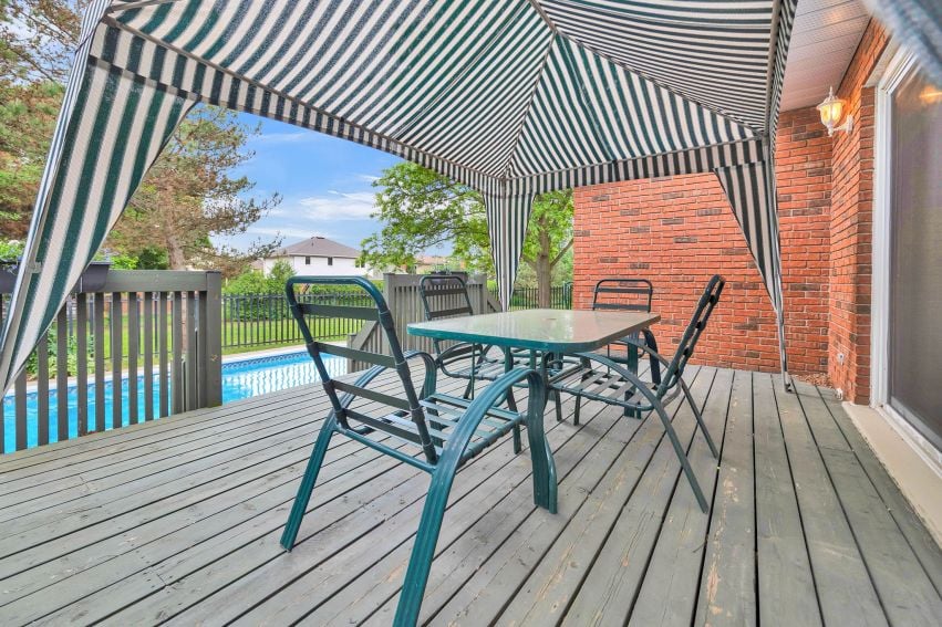 Wooden deck with a striped canopy, patio dining set, and fenced swimming pool.