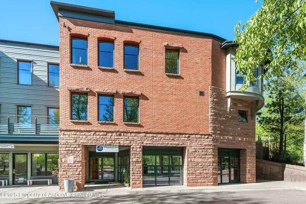 Aspen brick building with a stone-clad ground floor and large storefront windows.