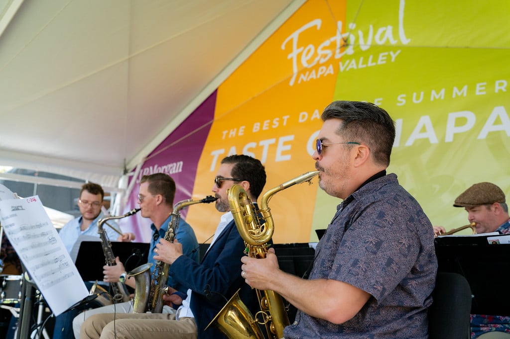 Musicians perform with saxophones and brass instruments beneath a Festival Napa Valley Taste of Napa banner.