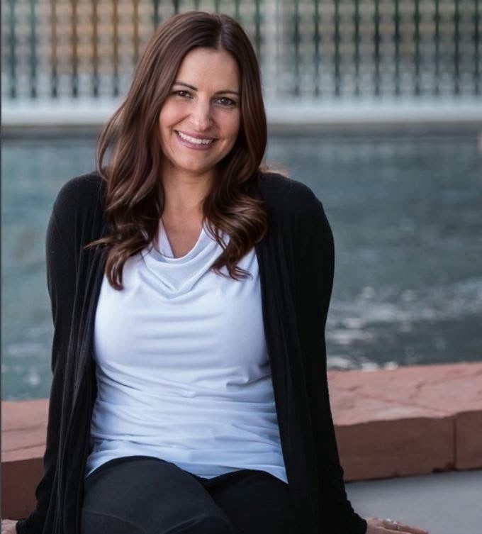 Sarah Ruiz seated beside a reflecting pool, wearing a white top and black cardigan.