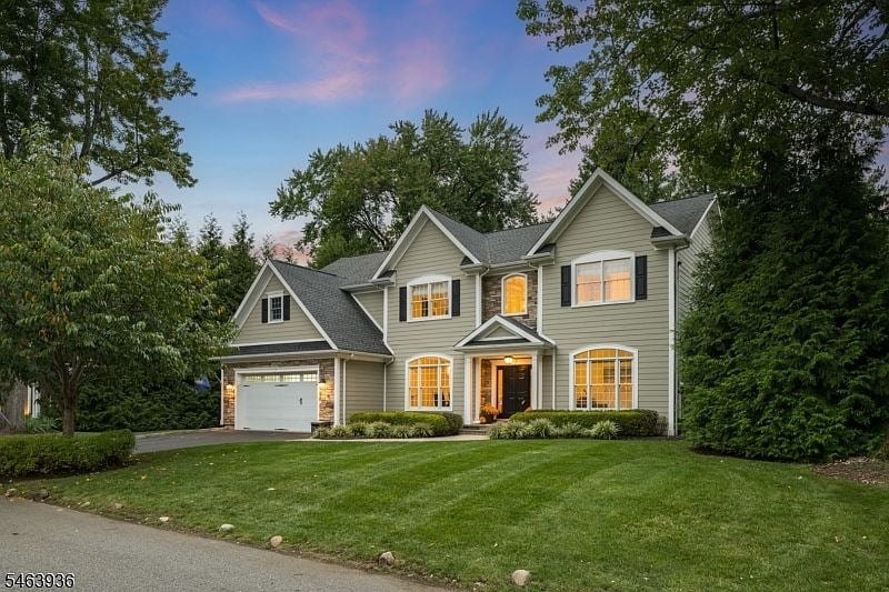 Two-story gray house with an attached garage, landscaped lawn, and mature trees at dusk.
