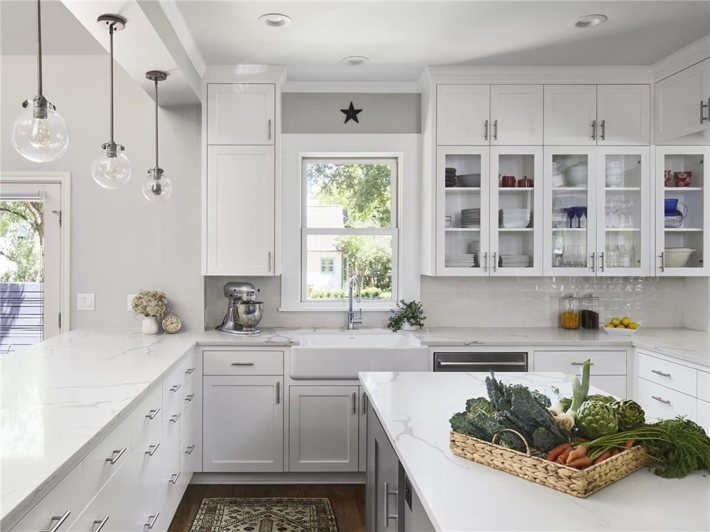 U-shaped kitchen with white shaker cabinetry, quartz countertops, a farmhouse sink, and glass-front upper cabinets, in a Pemberton Heights home on Northwood Road in Austin, Texas.