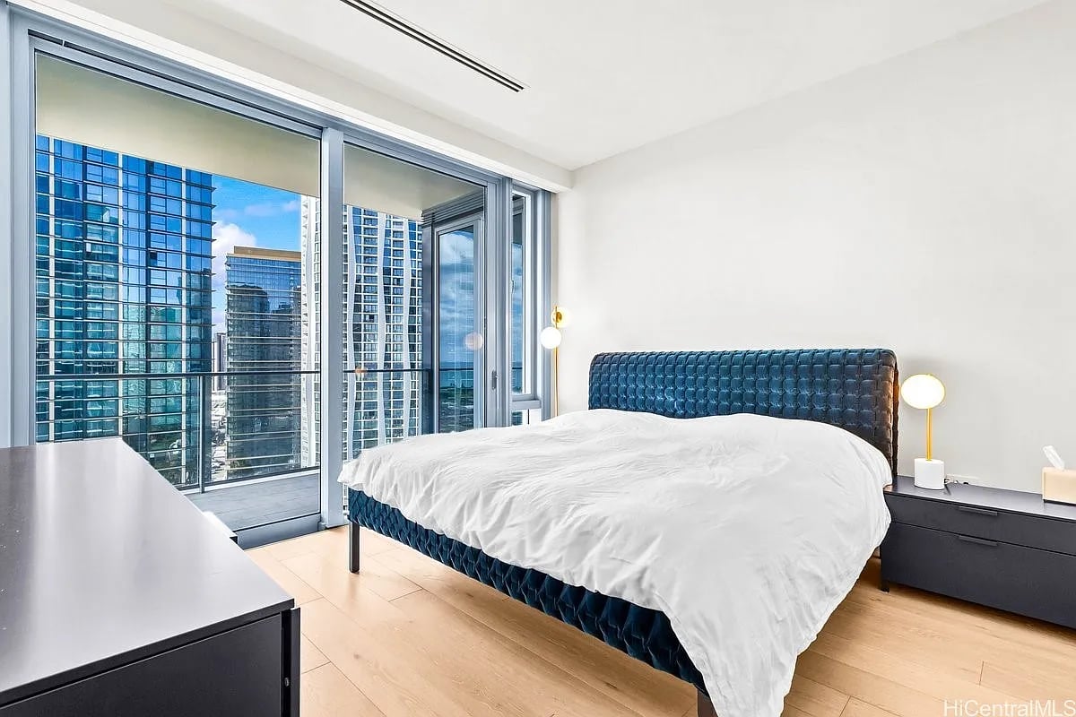 Bedroom with a blue upholstered bed and floor-to-ceiling windows overlooking the city skyline.