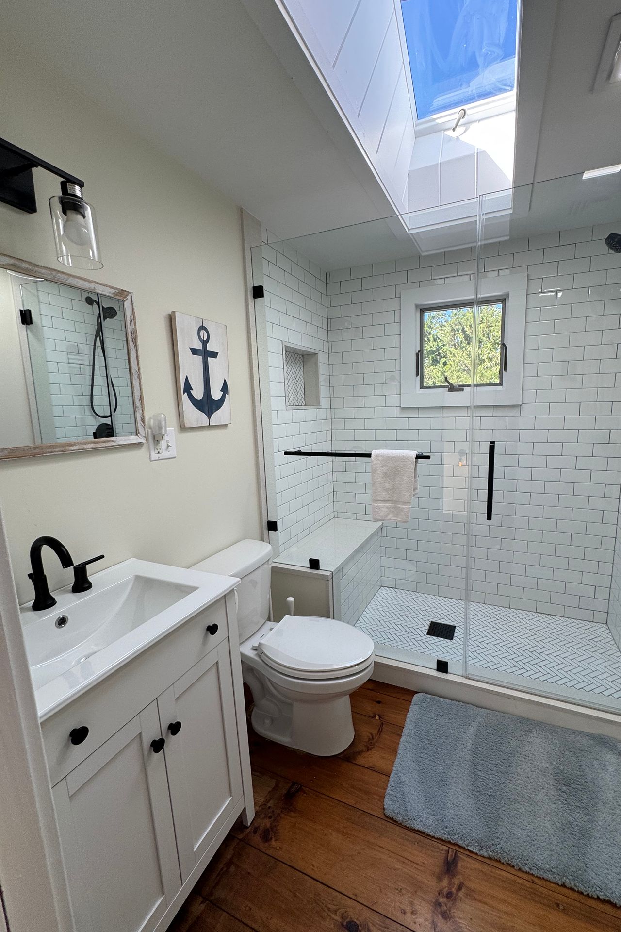 Bathroom with a glass-enclosed subway-tile shower, skylight, and white vanity.