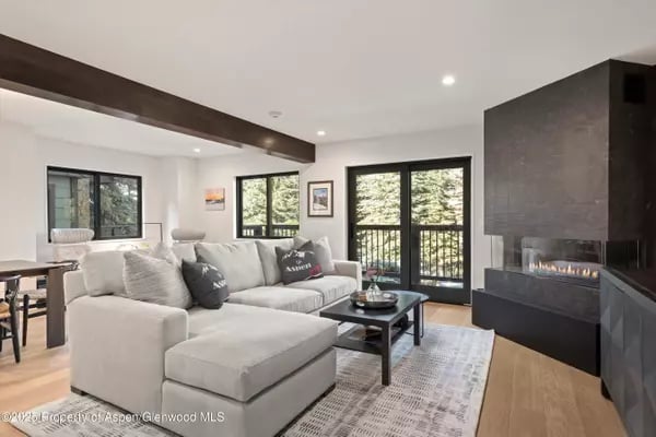 Contemporary living room with a large sectional, stone fireplace, and glass doors to a tree-lined balcony.