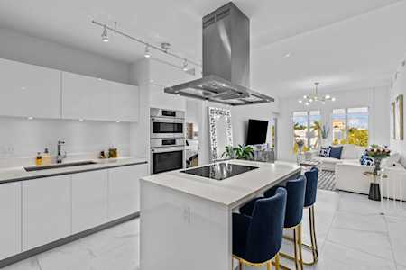 Open-plan kitchen with a large cooktop island and navy bar stools beside a bright living room.