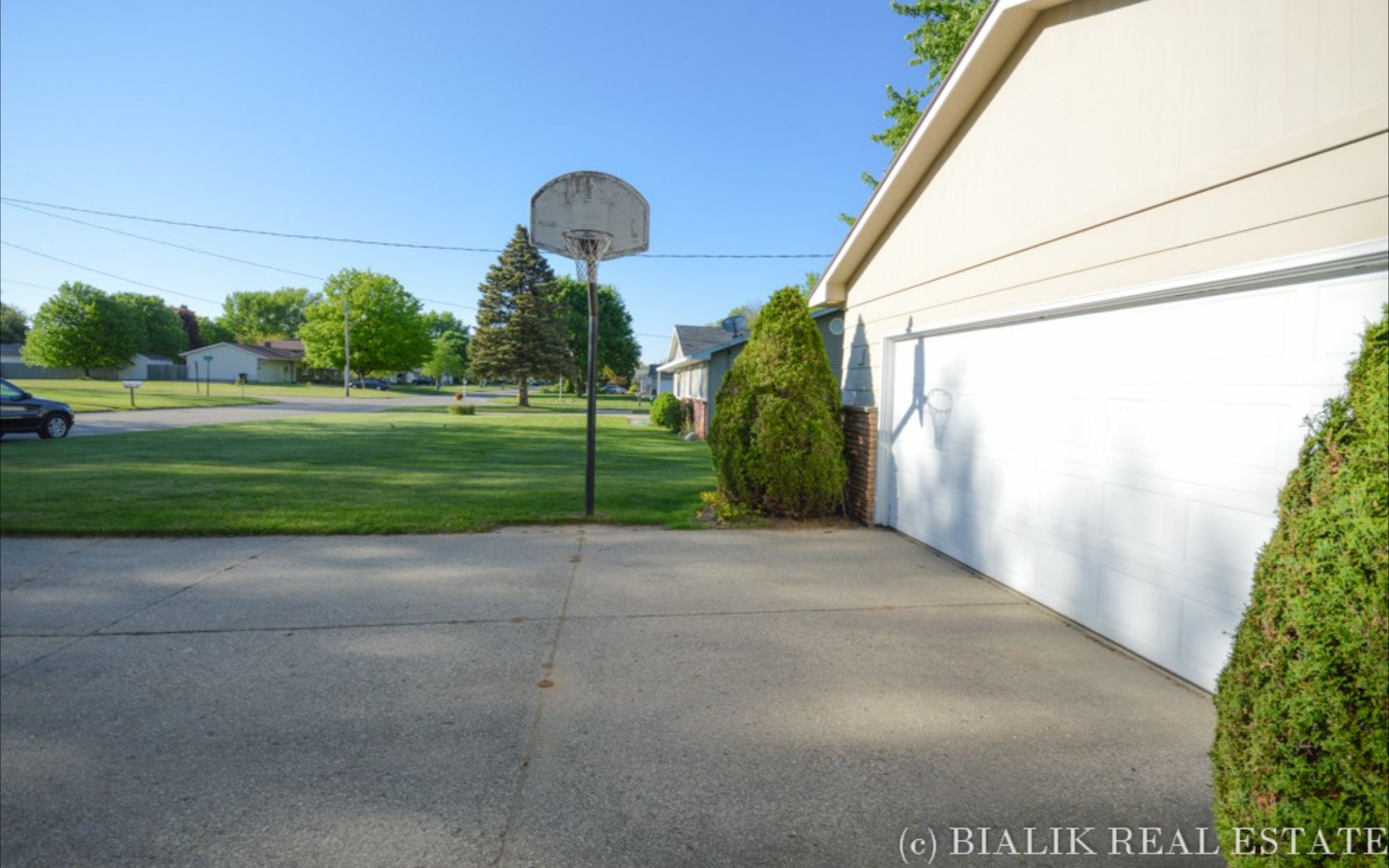 Suburban driveway and white garage beside a lawn with a basketball hoop.