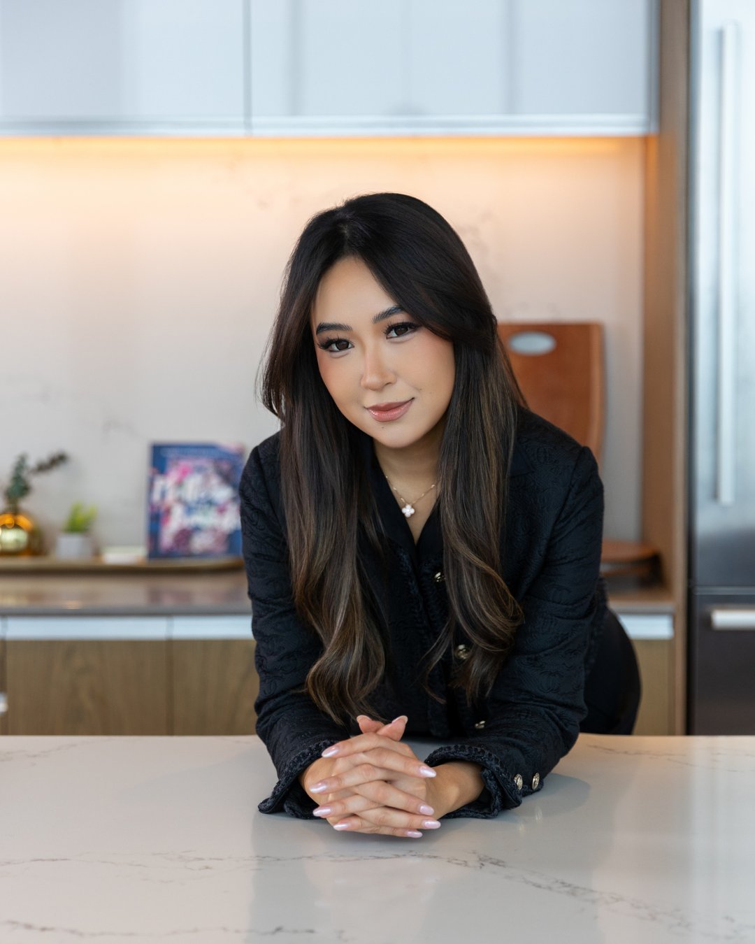 Fiona Jiao, West Bellevue luxury real estate advisor, leaning on a marble kitchen counter in a black jacket.