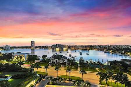 Waterfront neighborhood at dusk with palm-lined homes, boats, and docks along the water.