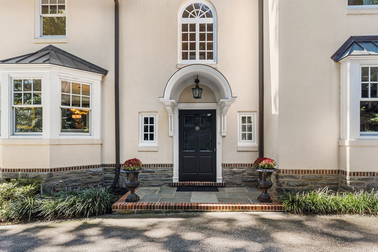 Home entrance with arched white trim, black door, stone foundation, and flower planters.