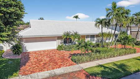 Single-story home with a red brick driveway, two-car garage, and palm trees in the front yard.