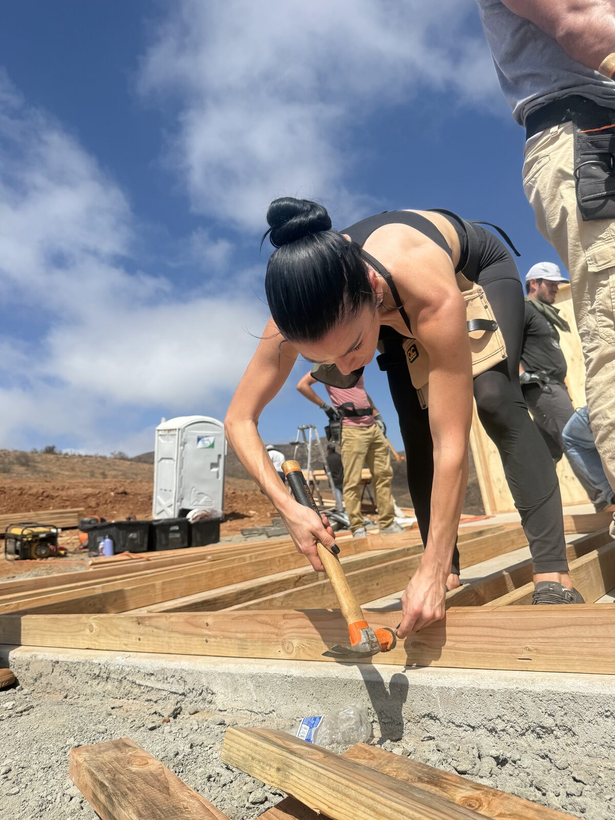 Jade Larney kneeling on the floor deck driving nails into the framing at the Baja build