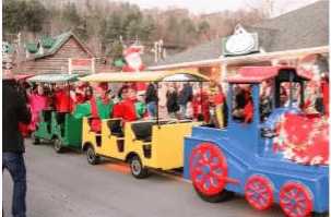 A colorful holiday parade train carries costumed riders past storefronts and spectators.