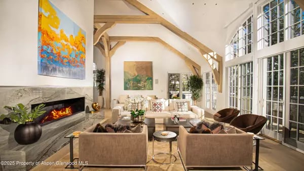 Living room with a stone fireplace, exposed timber beams, and tall grid-pane windows.