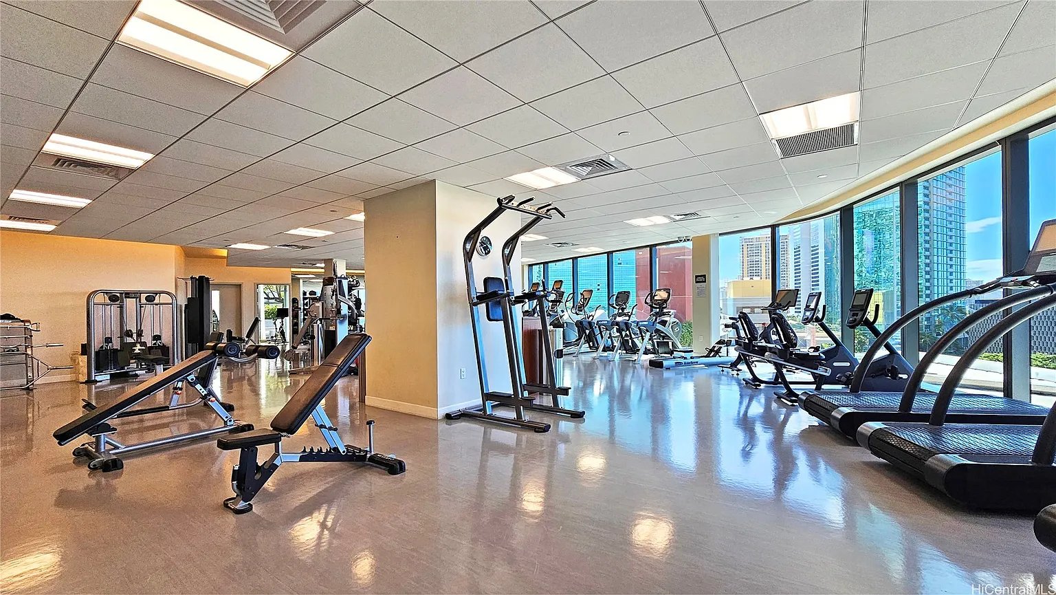 Fitness center with treadmills and weight equipment beside windows overlooking the city.