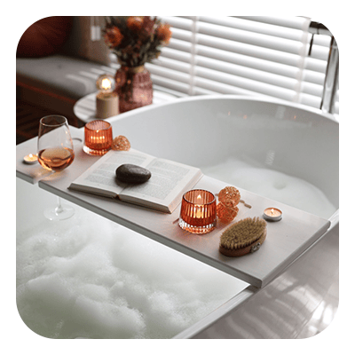 Soaking bathtub with a tray holding an open book, candles, wine, and a bath brush.