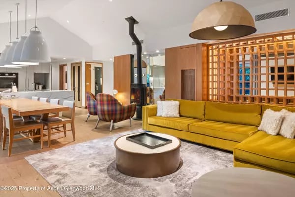 Open-plan living room with a mustard-yellow sofa, round coffee table, and black freestanding stove.