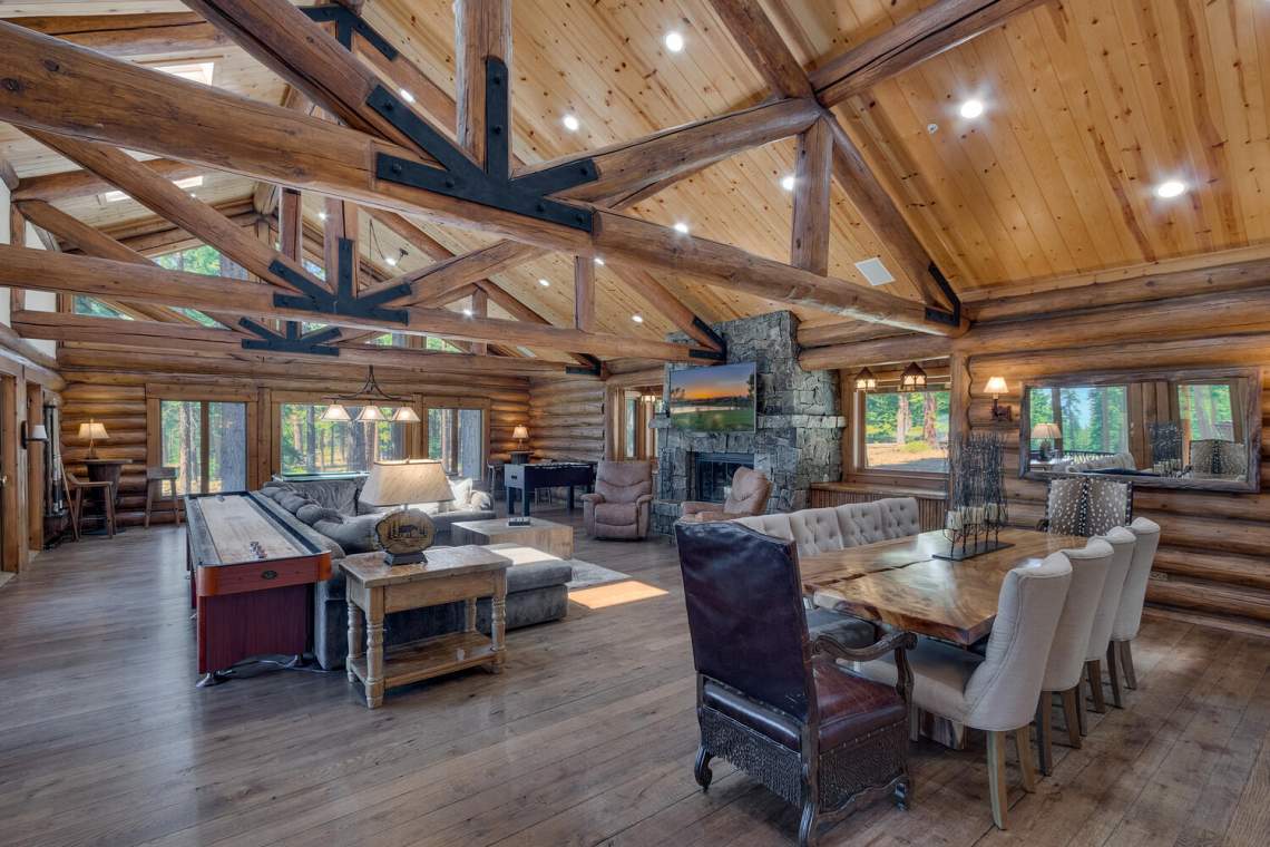 Log home great room with exposed timber trusses, a stone fireplace, and pool table.
