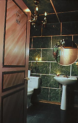 Bathroom with dark green marble tile, pedestal sink, and partially open paneled wooden door.