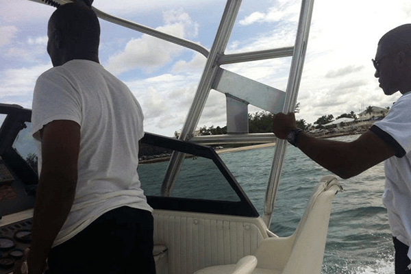 Two men aboard a motorboat on turquoise water, one steering and the other holding a metal frame.