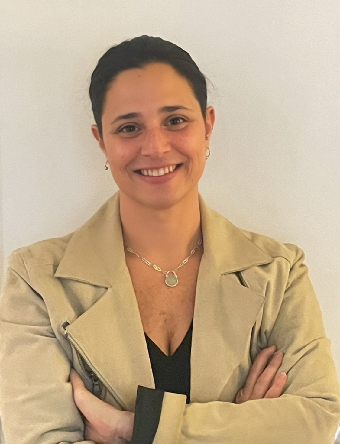 Toniann Ulses smiling with her arms crossed in a beige jacket.