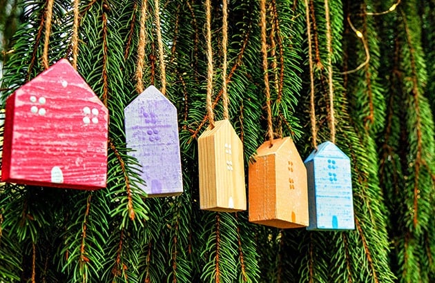 Colorful wooden house ornaments hang from an evergreen branch.