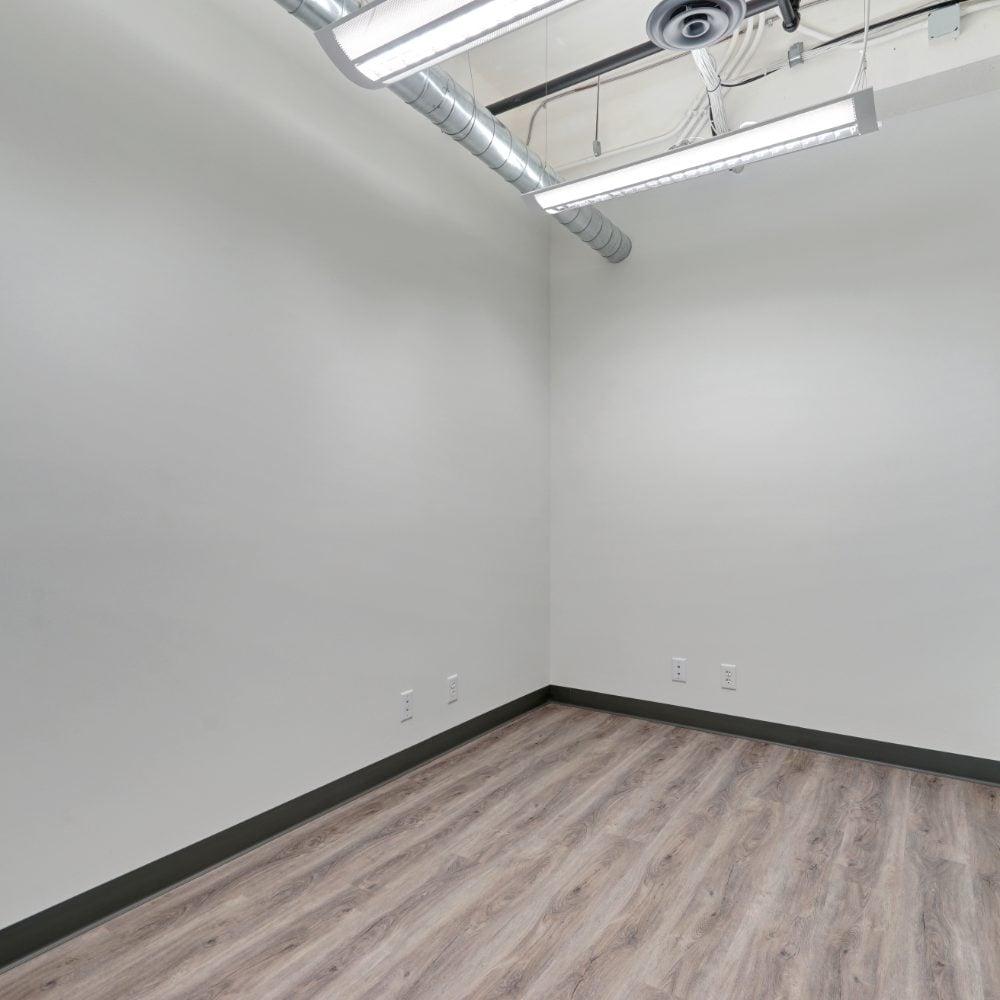 Empty room with wood-look flooring and exposed ceiling ductwork.