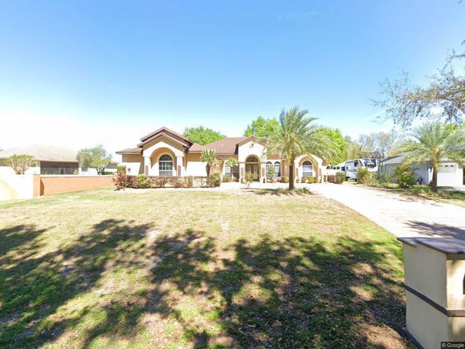 Single-story stucco home with arched windows, palm trees, and a broad front lawn.