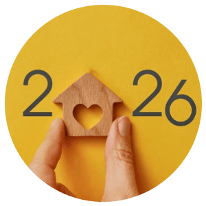 Hands hold a small wooden house with a heart-shaped opening beneath the year 2026.