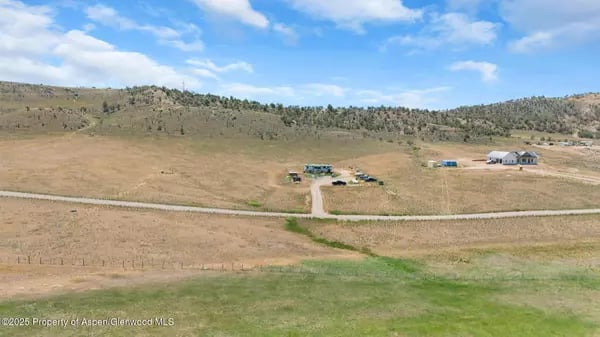 Open acreage with a dirt access road and scattered buildings, backed by low hills.