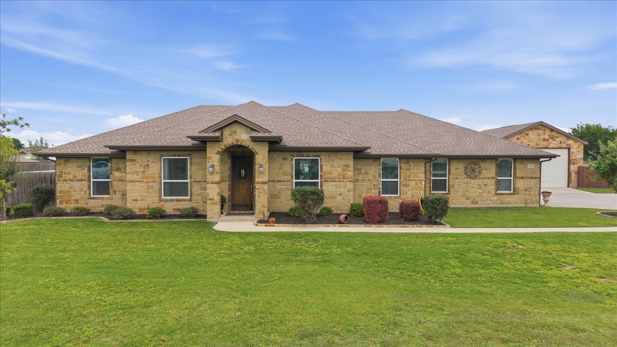 Single-story stone house with an arched entry, attached garage, and broad front lawn.