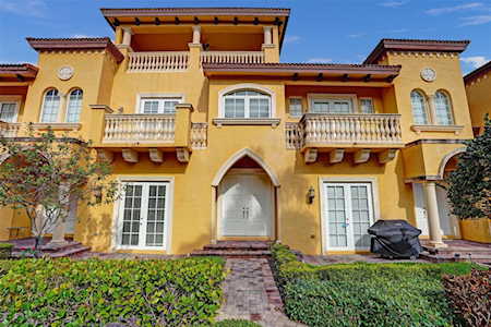 Yellow Mediterranean-style residence with arched entry, balconies, and landscaped front walkway.