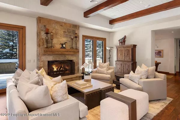Living room with a stone fireplace, exposed ceiling beams, and light upholstered seating.