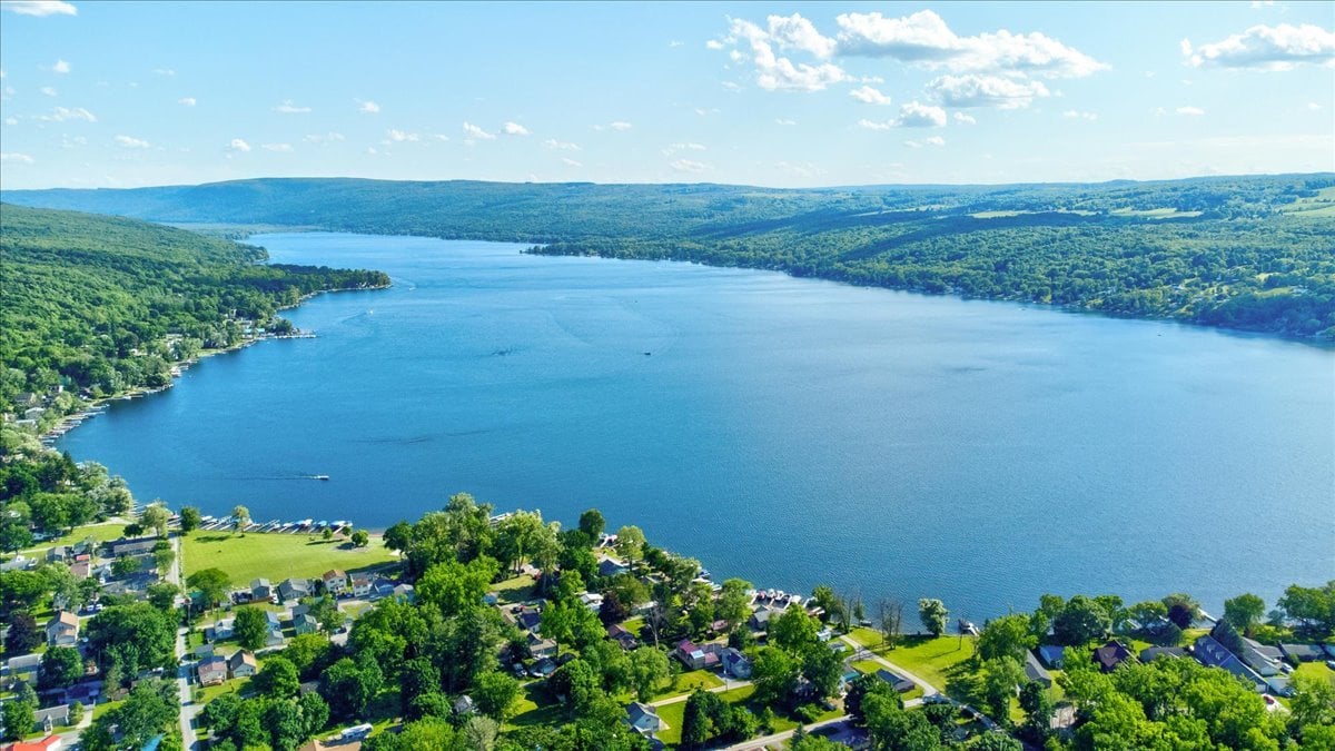 Aerial view of a lake and shoreline homes, with wooded hills in the distance.