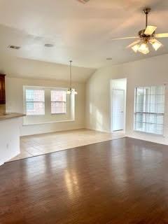Vacant living and dining area with hardwood floors, large windows, and a ceiling fan.