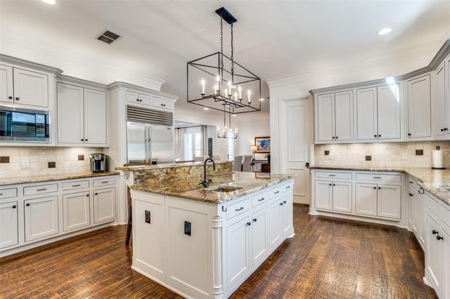 White kitchen with a large stone island, stainless steel appliances, and dark hardwood floors.