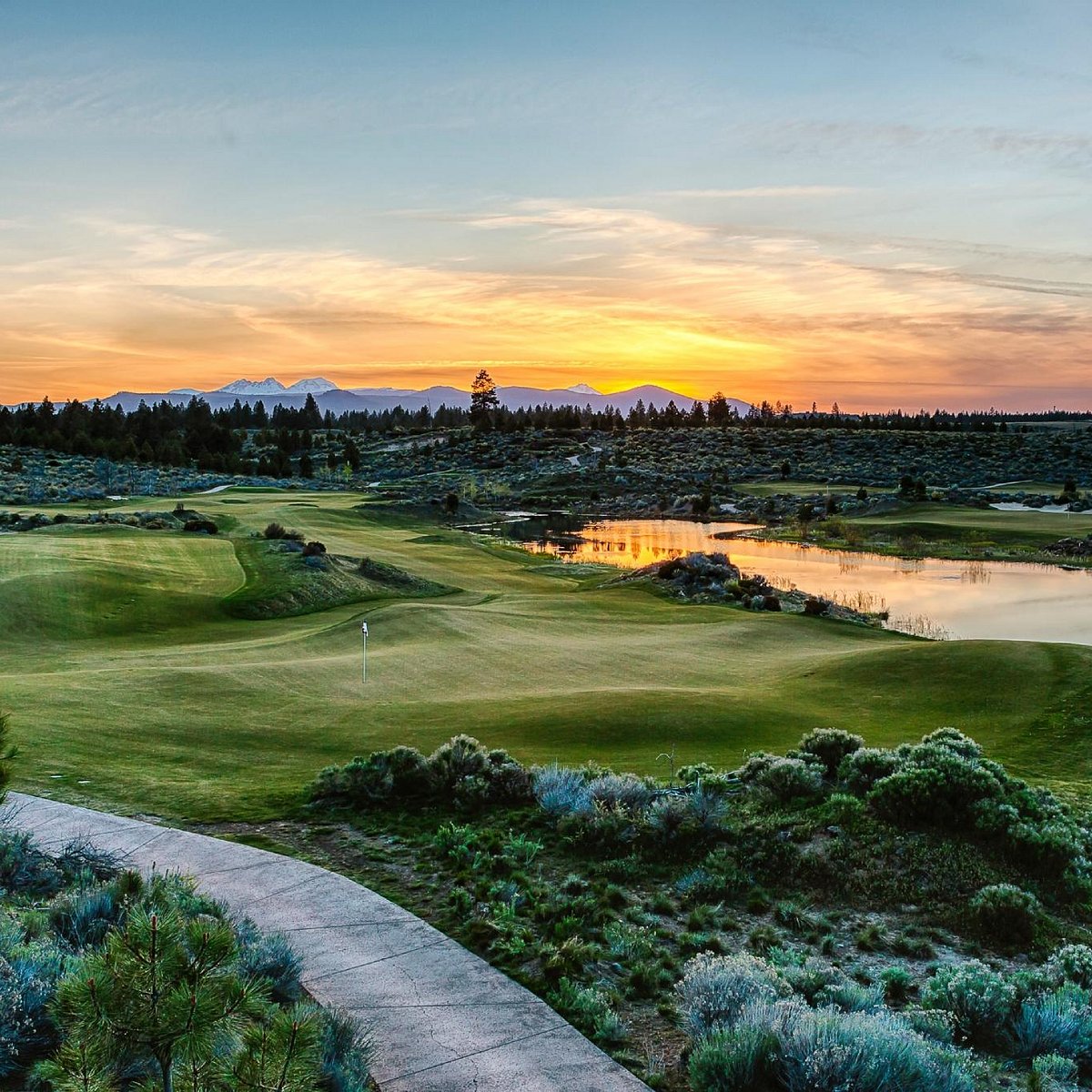 Tetherow golf course at sunset, with a reflective pond and mountain silhouettes on the horizon.