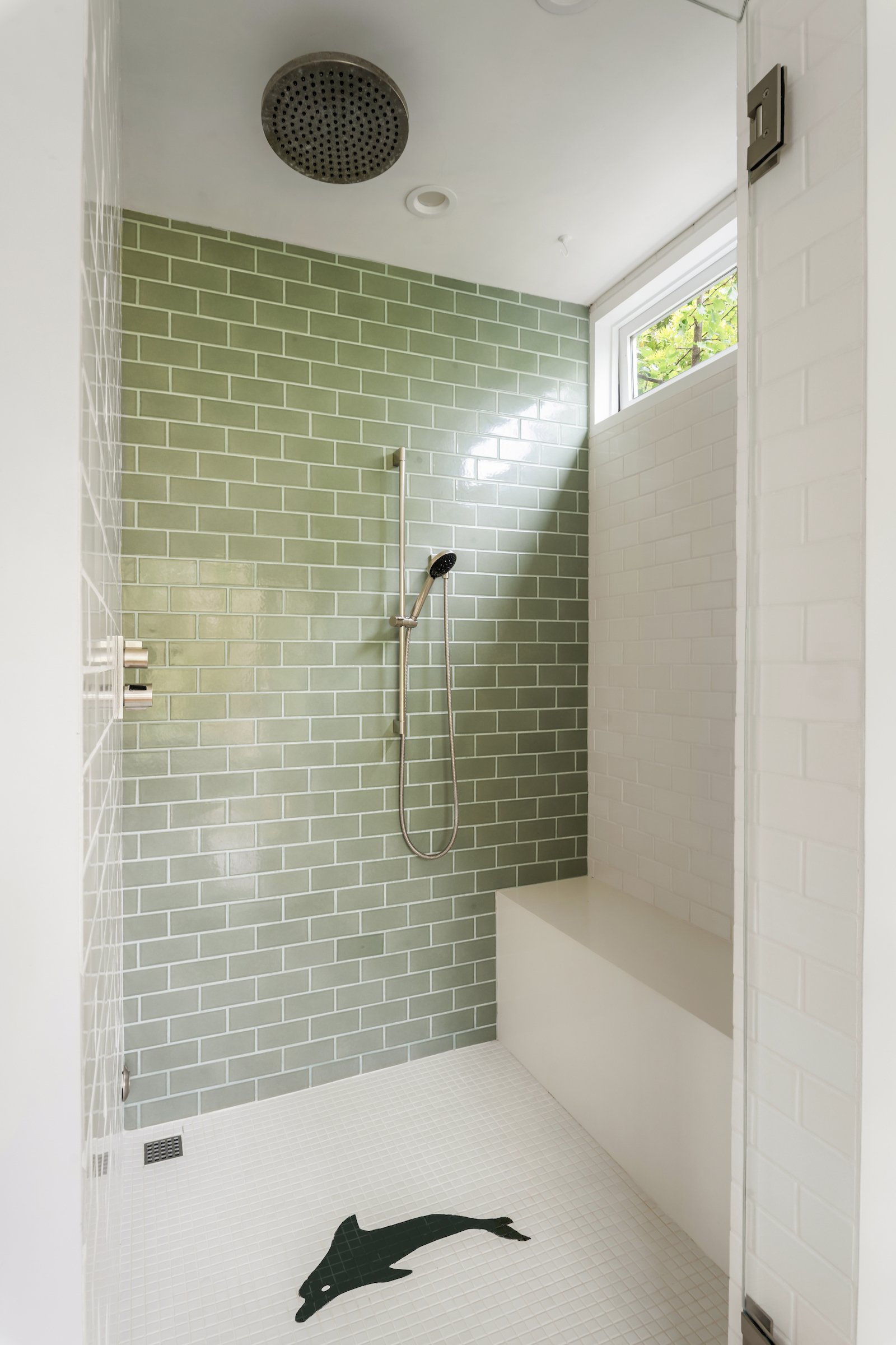 Walk-in shower with sage-green tile, a rain showerhead, built-in bench, and whale-shaped floor inlay.